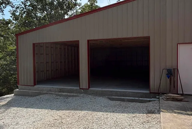 Completed shop extension, Alpena AR The completed extension in cream metal siding with red trim, two large open bays on a concrete floor and a gravel apron in front
