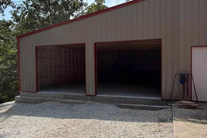 Completed shop extension, Alpena AR The completed extension in cream metal siding with red trim, two large open bays on a concrete floor and a gravel apron in front