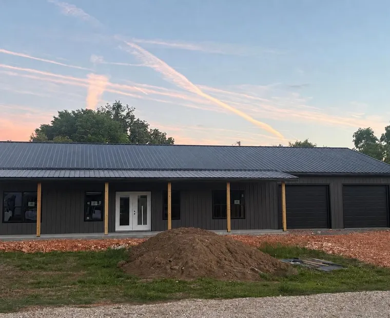 A completed post-frame home built by Sundown, dark metal walls and roof with a covered porch and twin garage bays