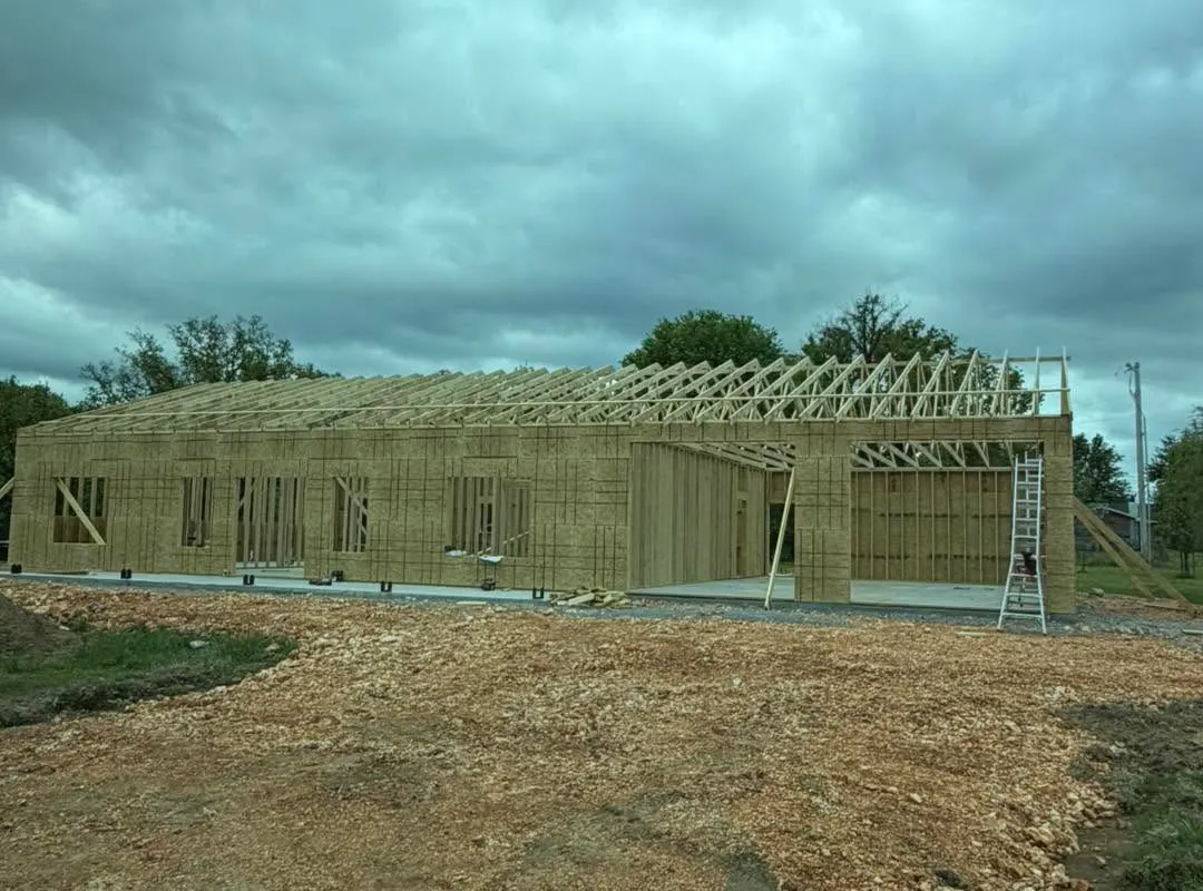 Barndominium framing, Fayetteville AR Timber framing and roof trusses set on a concrete slab, walls sheathed in OSB, under a grey sky