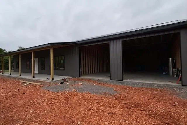 Metal cladding going on, Fayetteville AR The same building clad in dark metal siding with the roof on, two garage bays still open and the covered porch posts in bare timber
