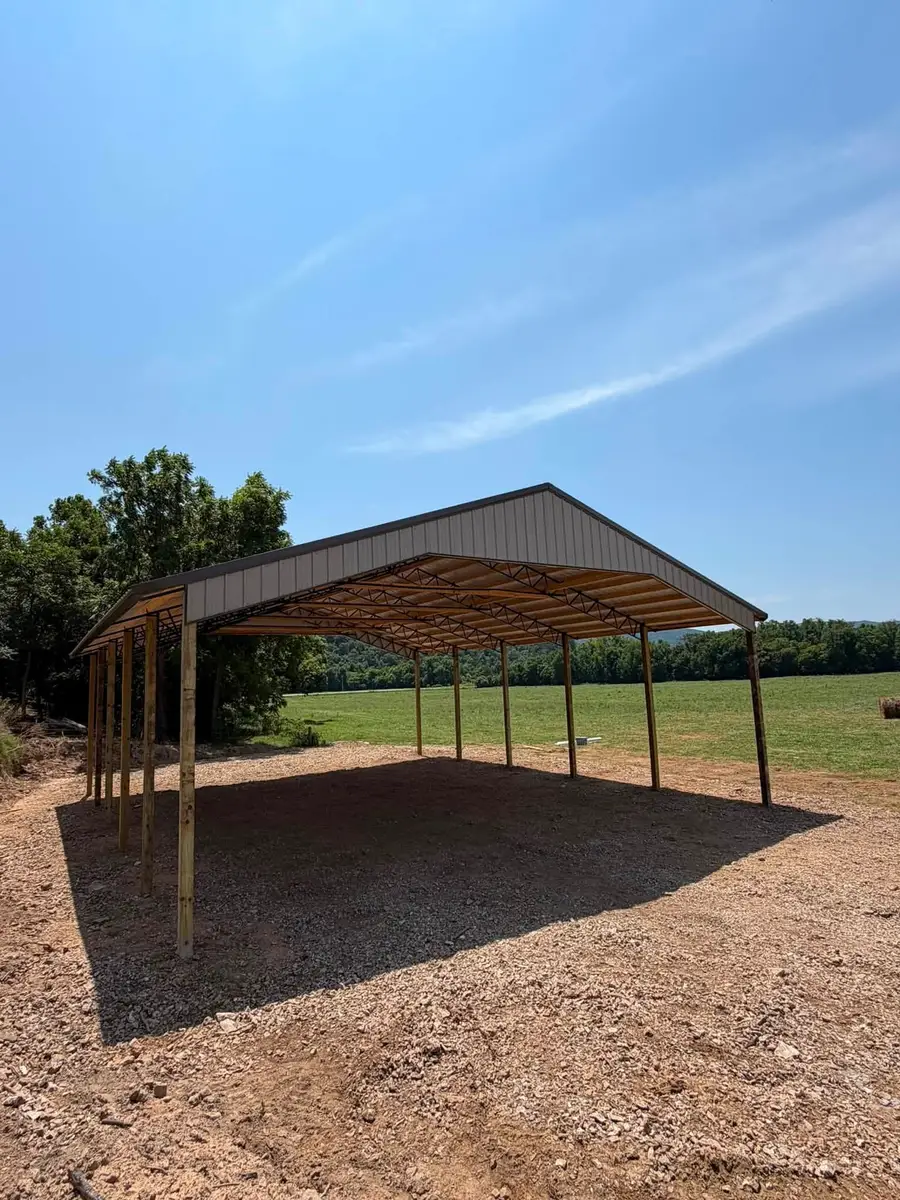 Pole Barn Construction A wide open-sided post-frame shelter with timber posts and a metal gable roof, looking through to pasture