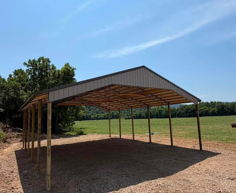 Pole Barn Construction A wide open-sided post-frame shelter with timber posts and a metal gable roof, looking through to pasture